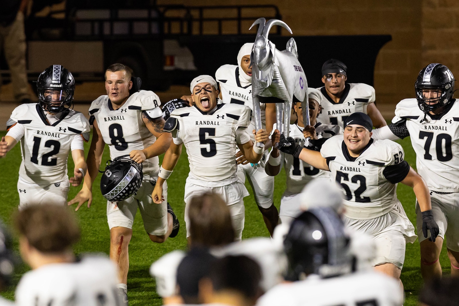 RHS-CHS-FB-39 | Press Pass Sports Randall football team celebrates victory on field, lifting a silver horse trophy together.
