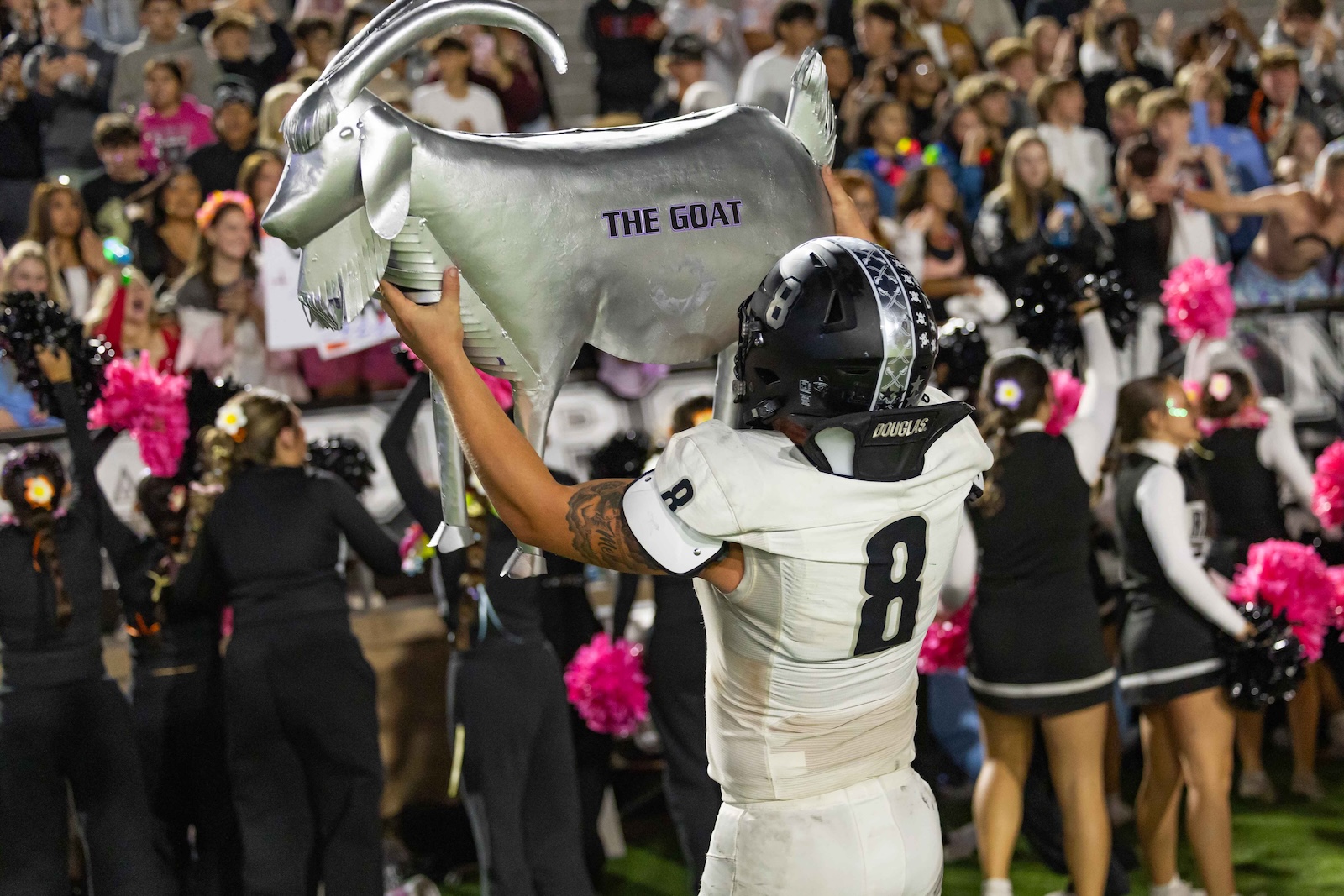 RHS-CHS-FB-41 | Press Pass Sports A football player in white uniform lifts a large silver goat trophy labeled 'THE GOAT' amid a cheering crowd and cheerleaders.