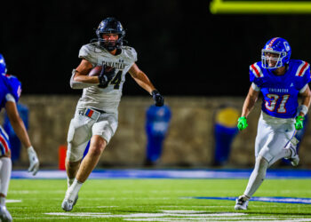 CT9A4515 | Press Pass Sports A football player in a white Canadian jersey runs with the ball on a night game while defenders in blue close in behind him.