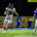CT9A4515 | Press Pass Sports A football player in a white Canadian jersey runs with the ball on a night game while defenders in blue close in behind him.