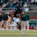 2C5A8014 | Press Pass Sports Football player in a black jersey (number 25) runs with the ball during a game, with a blurred crowd in the stands behind him, on a grass field.
