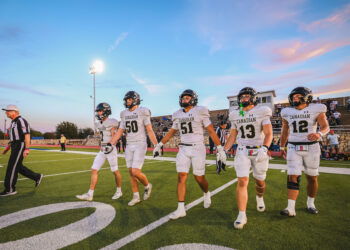 DEP21156 | Press Pass Sports Canadian football players in white uniforms walk off the field together as a referee looks on, with bleachers and a sunset sky in the background