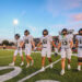DEP21156 | Press Pass Sports Canadian football players in white uniforms walk off the field together as a referee looks on, with bleachers and a sunset sky in the background