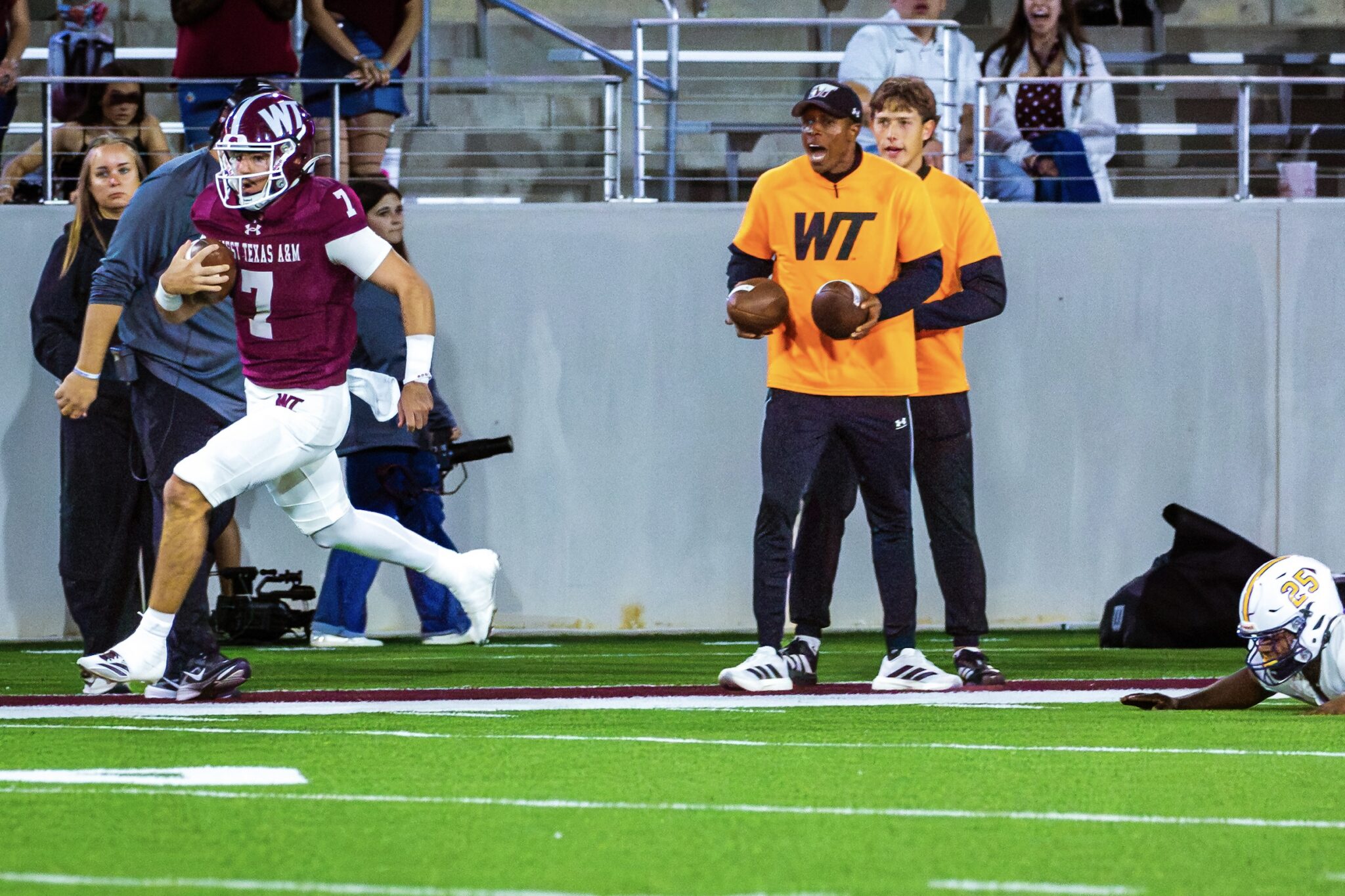 _V4A3285 1 | Press Pass Sports Maroon-clad football player with the ball sprints past on the field as orange-clad staffers stand by the sideline.