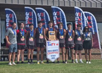 9550 | Press Pass Sports Group of boys in gray and black cross‑country uniforms wearing medals, posing with a banner that says CROSS COUNTRY CHAMPION behind them.
