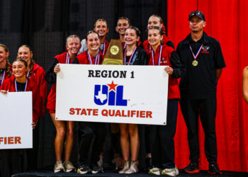 DEP29814 | Press Pass Sports Group of young athletes on a stage in red and black jackets, smiling with medals, holding a trophy and a Region 1/State Qualifier banner against red curtains and a black backdrop.
