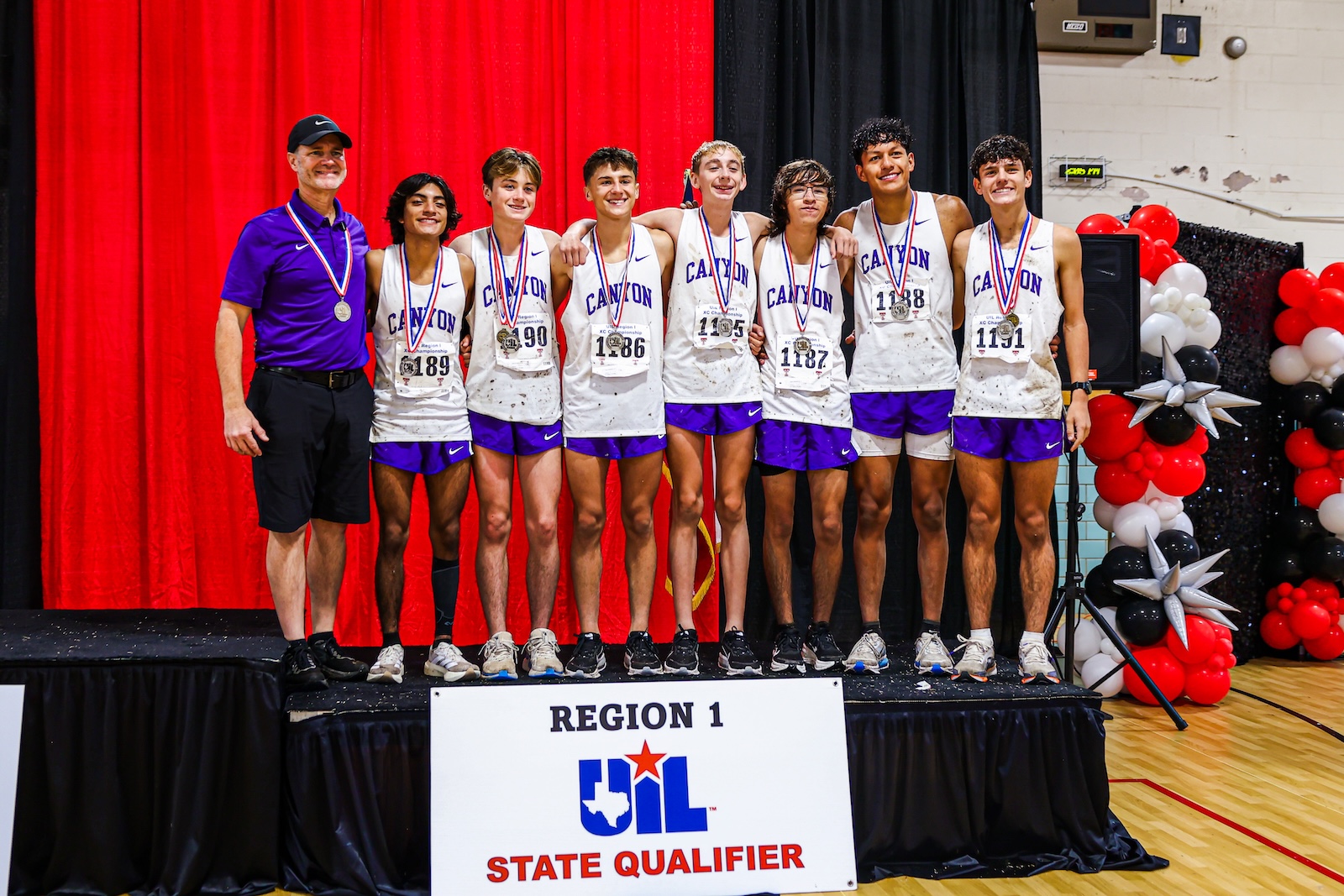 Coaching staff and nine athletes pose on stage with medals after a UIL state qualifier win, wearing white Canyon jerseys and purple shorts. Regional banner reads UIL State Qualifier in the foreground.