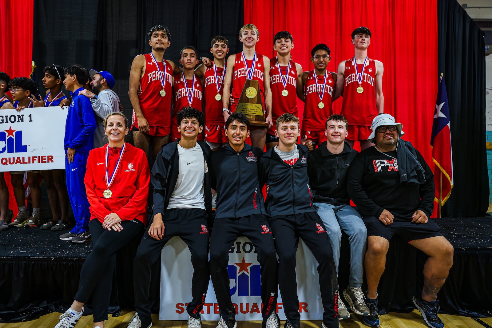 High school basketball team posing on stage with medals and a trophy, red uniforms, group photo after a regional qualifier win