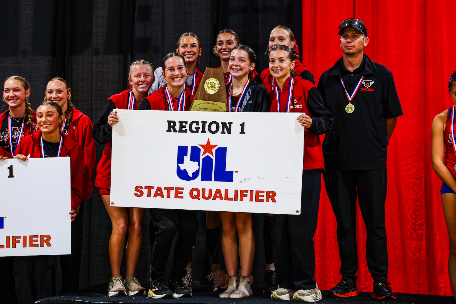 DEP29814 | Press Pass Sports Group of young athletes on a stage holding a Region 1 UIL State Qualifier banner with medals and a trophy.