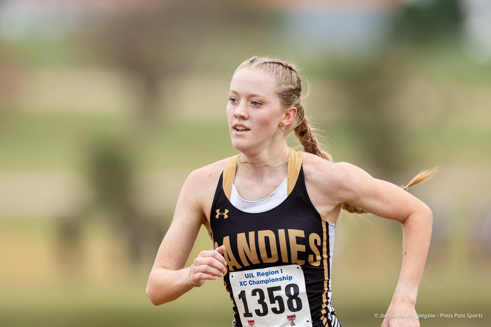 regional-xc-lubbock-2026-jpegJoe-pps-3 | Press Pass Sports Female cross-country runner in black and gold uniform mid-race, bib number 1358, outdoors.