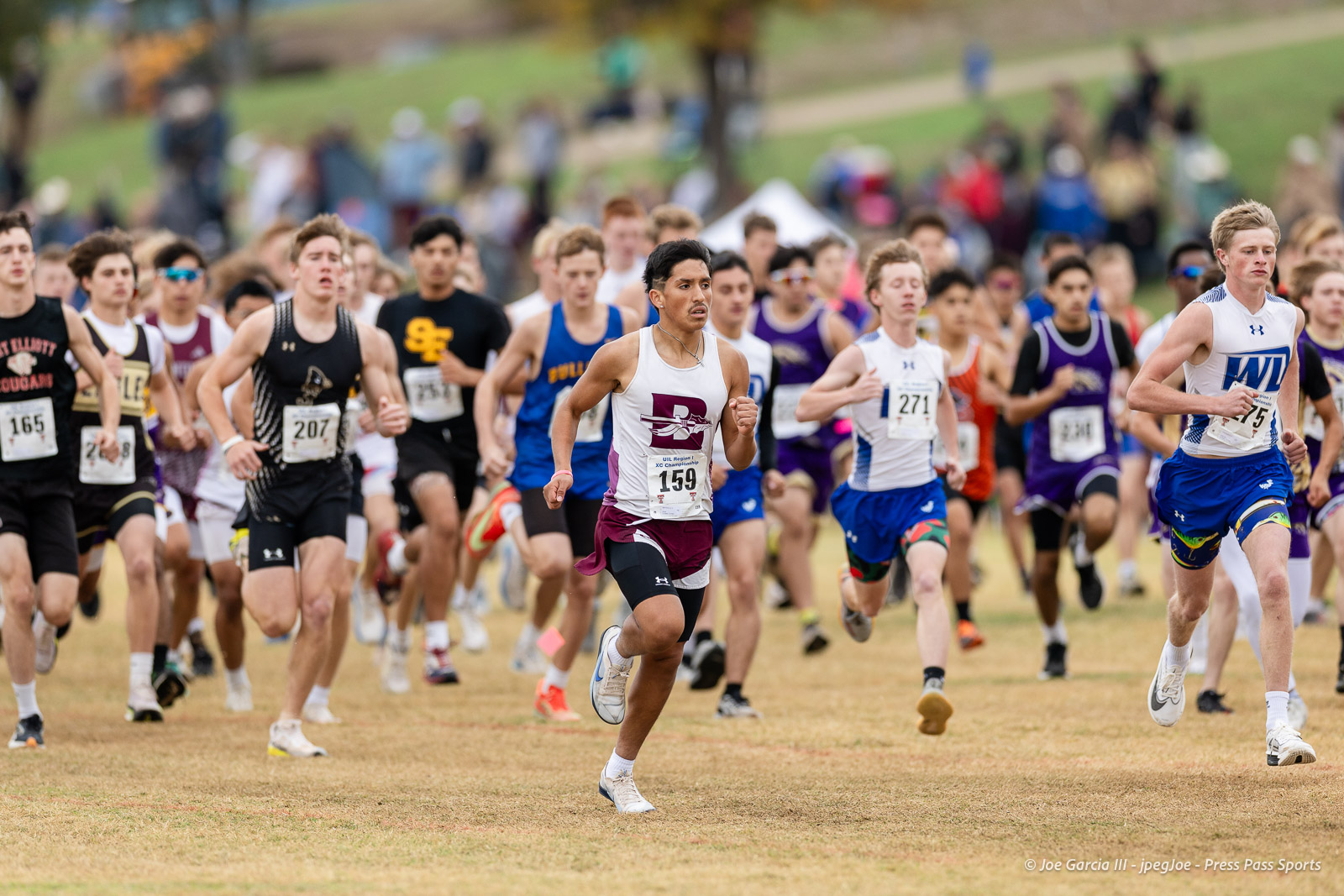 regional-xc-lubbock-2026-jpegJoe-pps-13 | Press Pass Sports Crowded cross-country race on a grassy field; foreground runner in white/maroon with bib 159 leads a large pack.