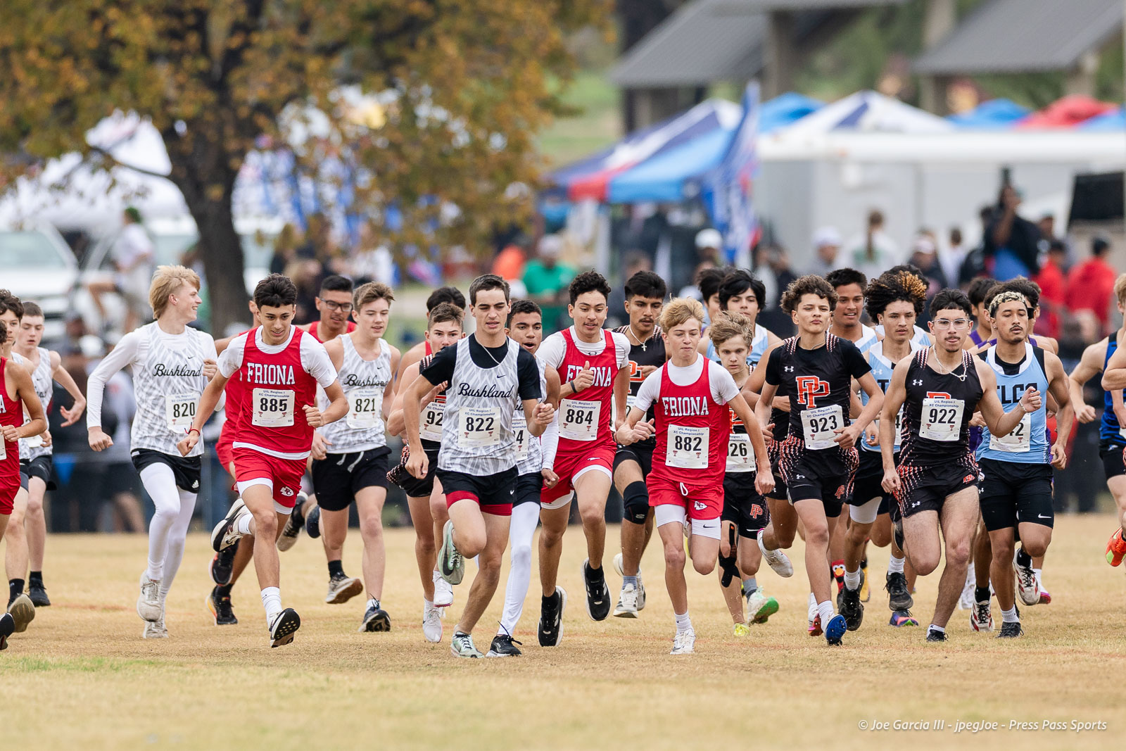 regional-xc-lubbock-2026-jpegJoe-pps-20 | Press Pass Sports Group of middle- and high-school runners sprint off at the start of a cross-country race on a grassy field in red, white, and black uniforms.