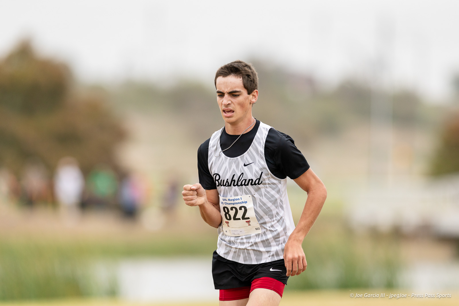 regional-xc-lubbock-2026-jpegJoe-pps-22 | Press Pass Sports Male runner in a gray-patterned singlet and black shirt, race bib 822, sprinting on a course outdoors with a focused expression.