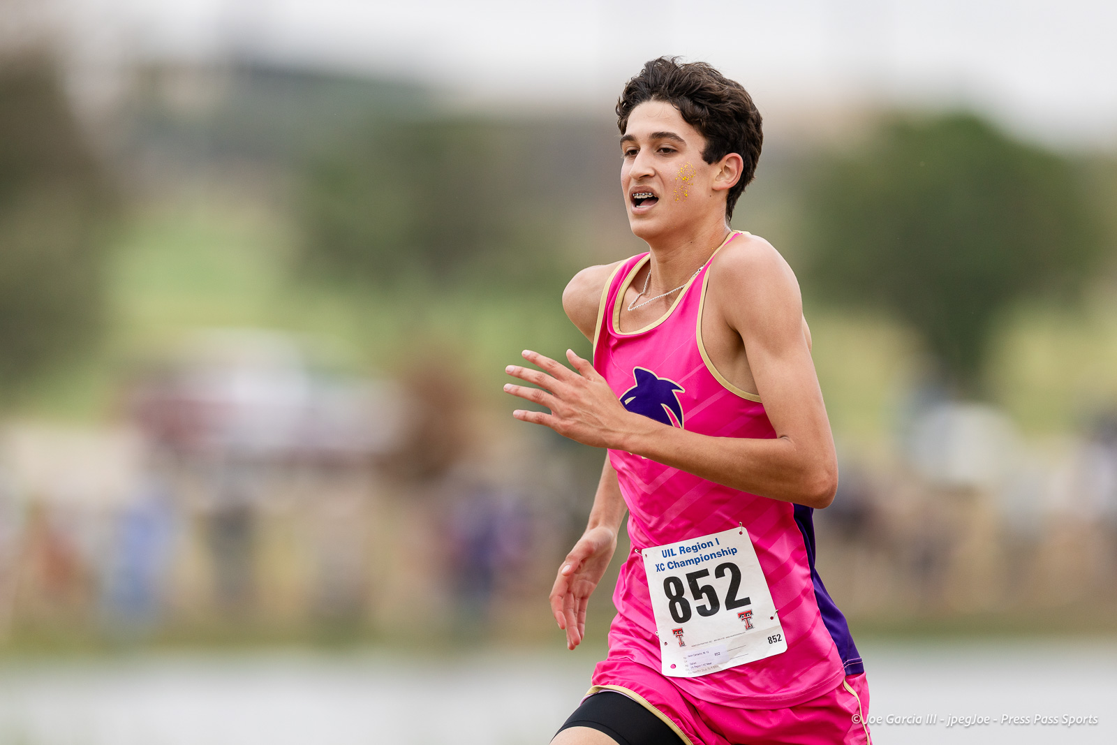 regional-xc-lubbock-2026-jpegJoe-pps-27 | Press Pass Sports Female runner in a bright pink singlet with bib 852 sprinting outdoors, against a blurred background.