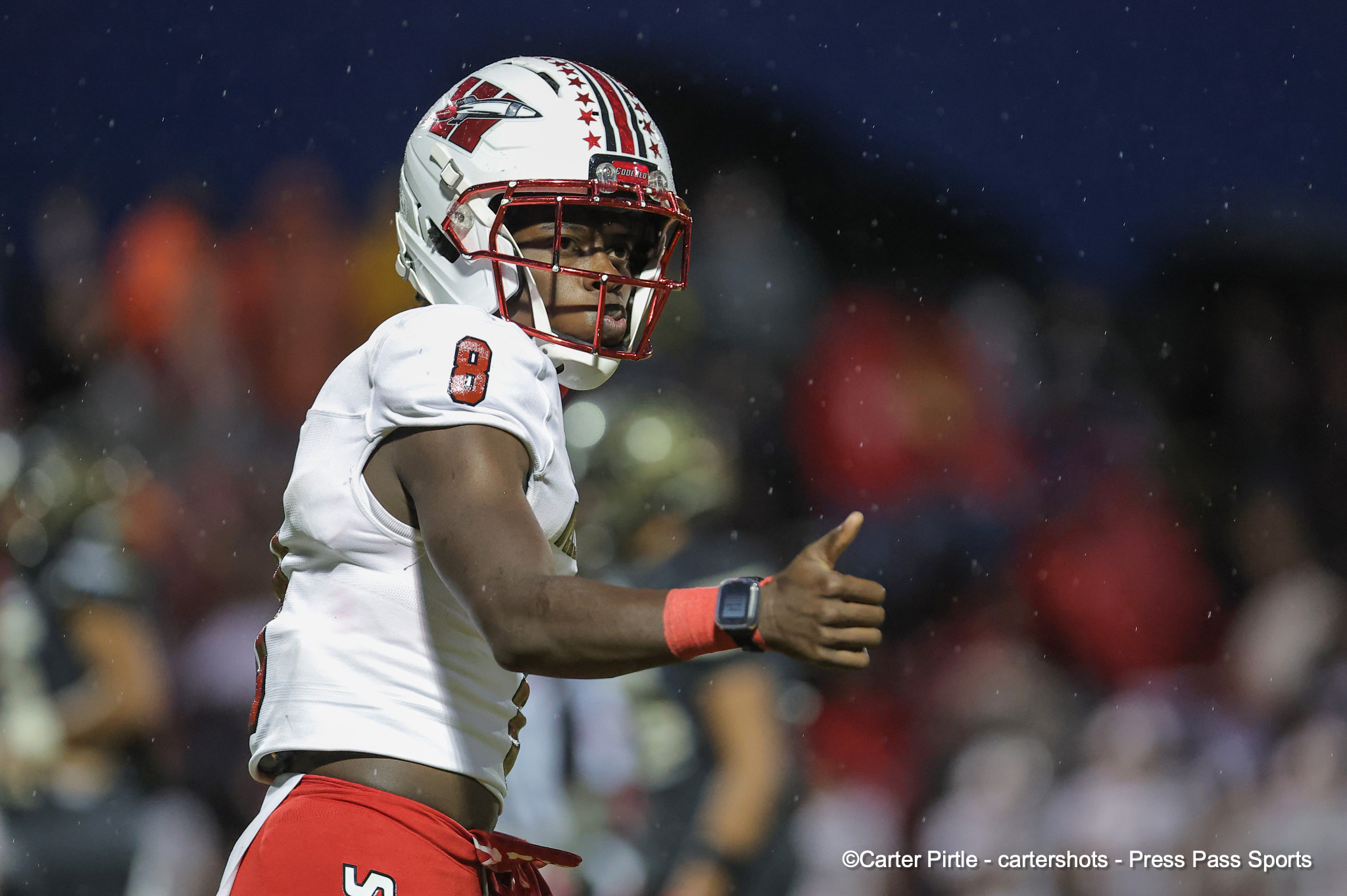 Football player in a white jersey and red pants celebrating with an arm raised on a snowy night game.