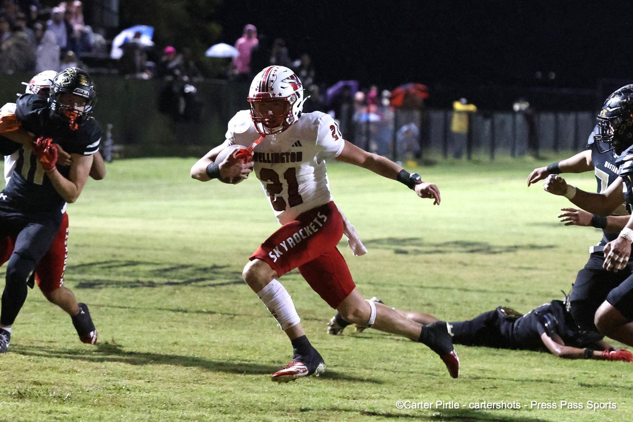 Football player in white jersey (number 31) running with ball during a nighttime game, defenders closing in on a grassy field