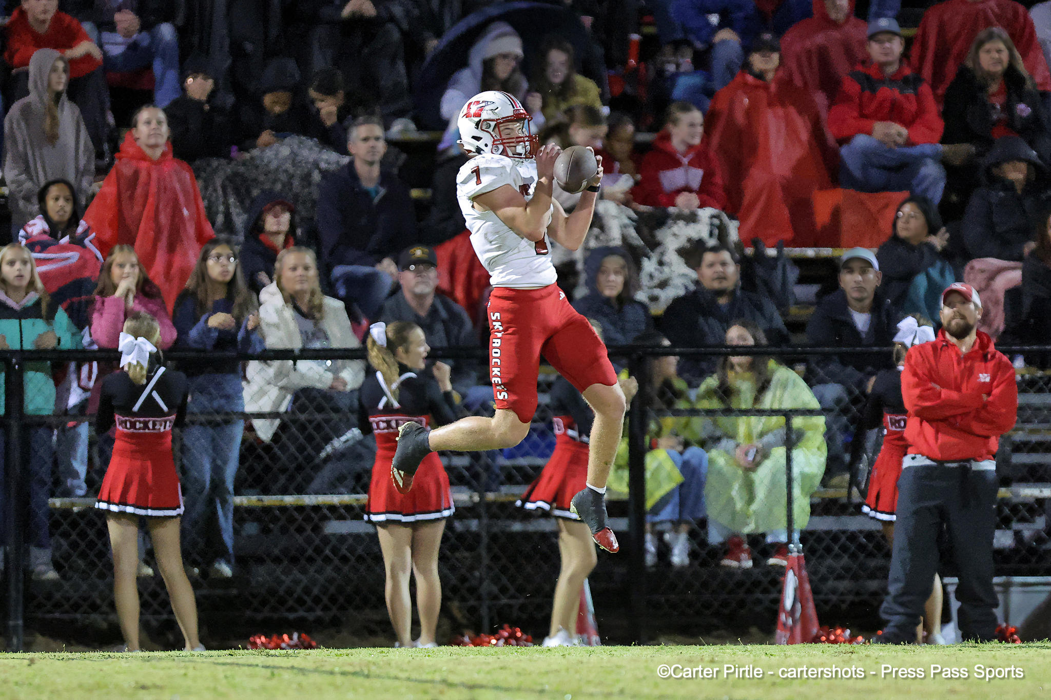 Football player in white jersey (#1) catches a pass in mid-air while crowds watch from stands in evening light.