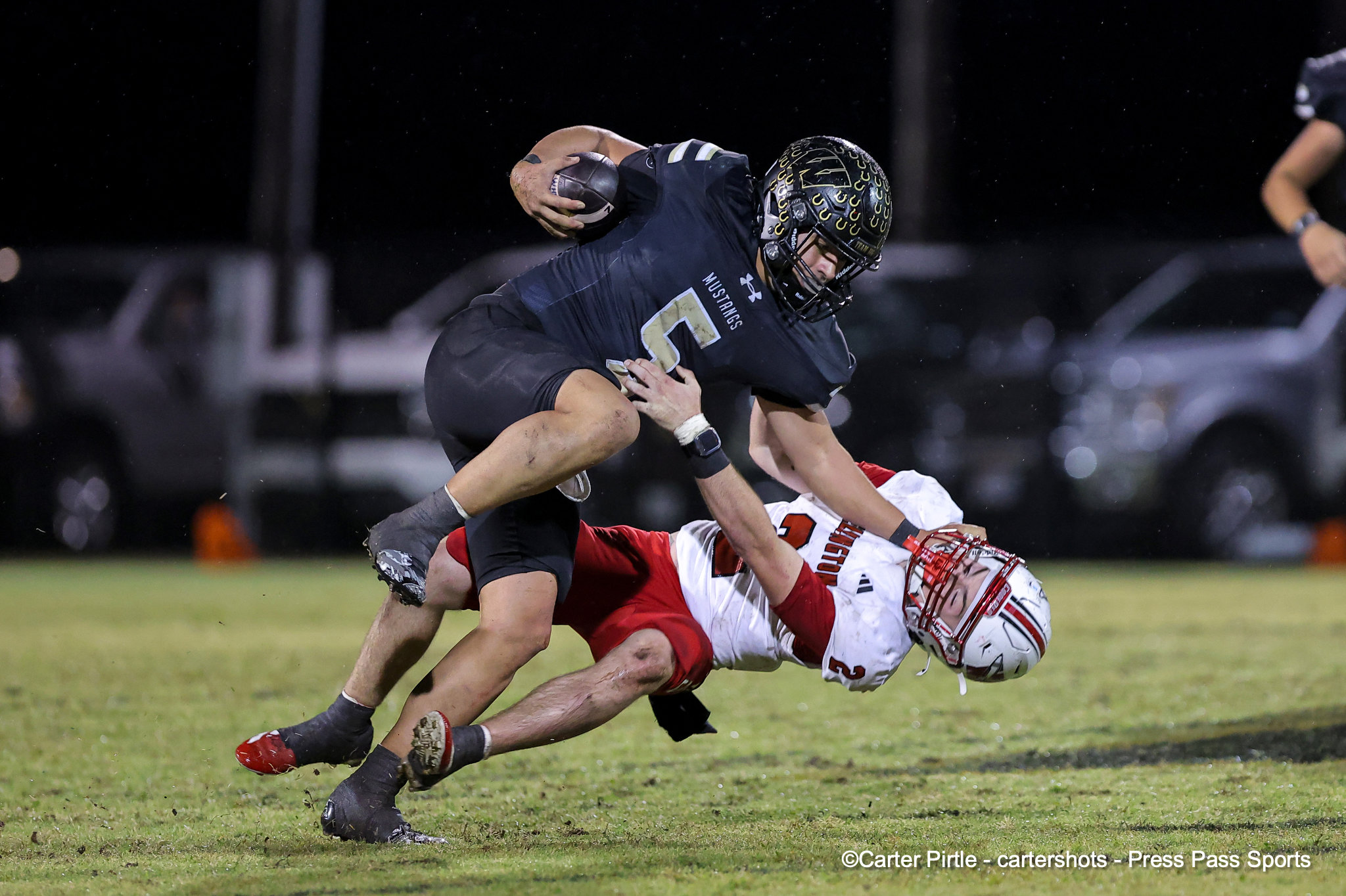 Nighttime football play: a navy-clad ball carrier (number 7) breaks free while being tackled by a defender in white and red, holding the ball close.