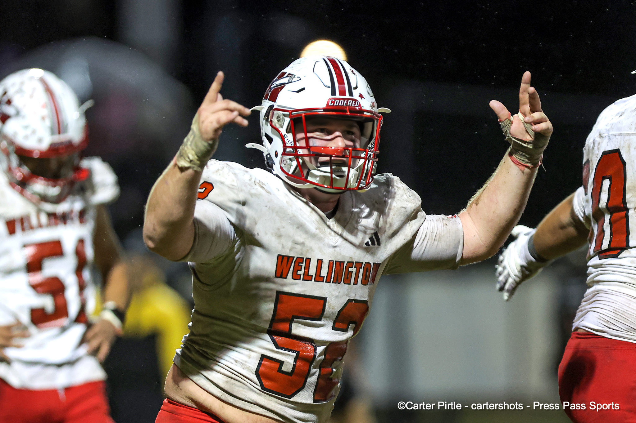 Wellington football player in a white jersey with orange number celebrating with raised arms.