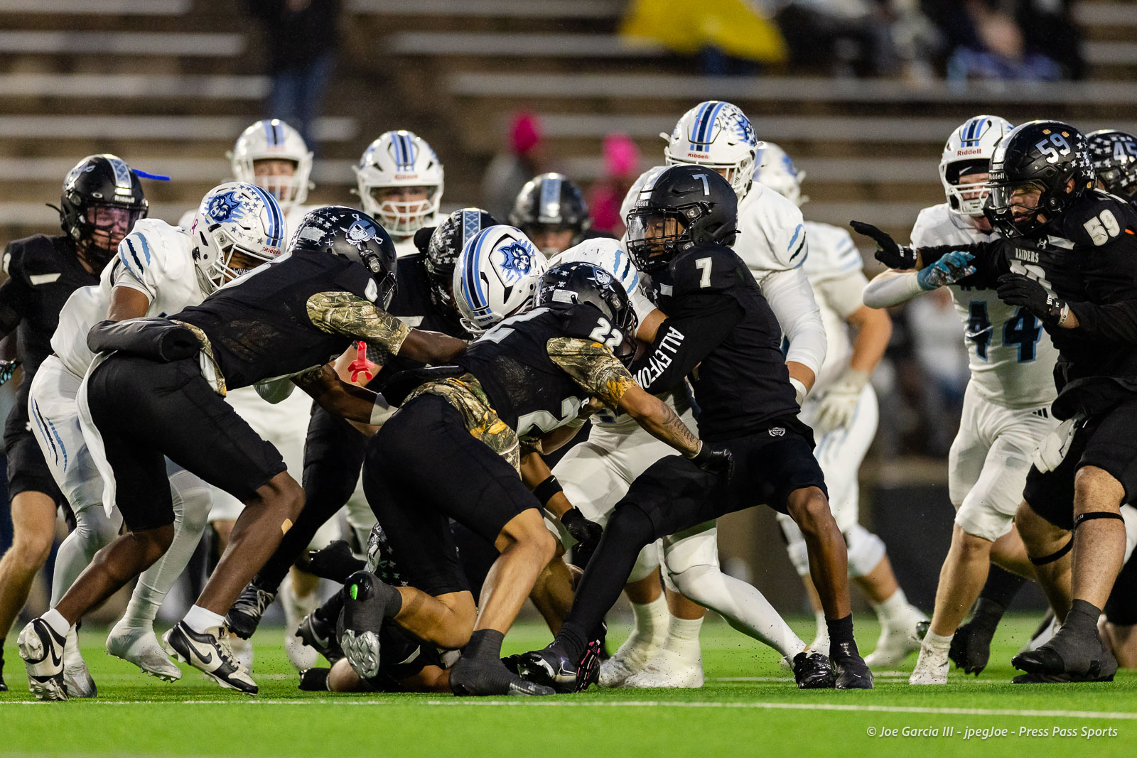 west-plains-vs-randall-2026-jpegJoe-pps-1 | Press Pass Sports Football players in white and black uniforms collide in a crowded pile on a green turf during a game.
