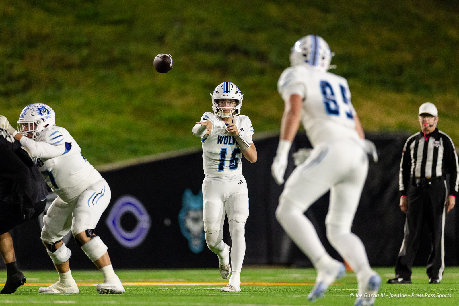 west-plains-vs-randall-2026-jpegJoe-pps-4 | Press Pass Sports Quarterback in white uniform throws a pass during a nighttime football game, teammates and a referee in the background on a green field.