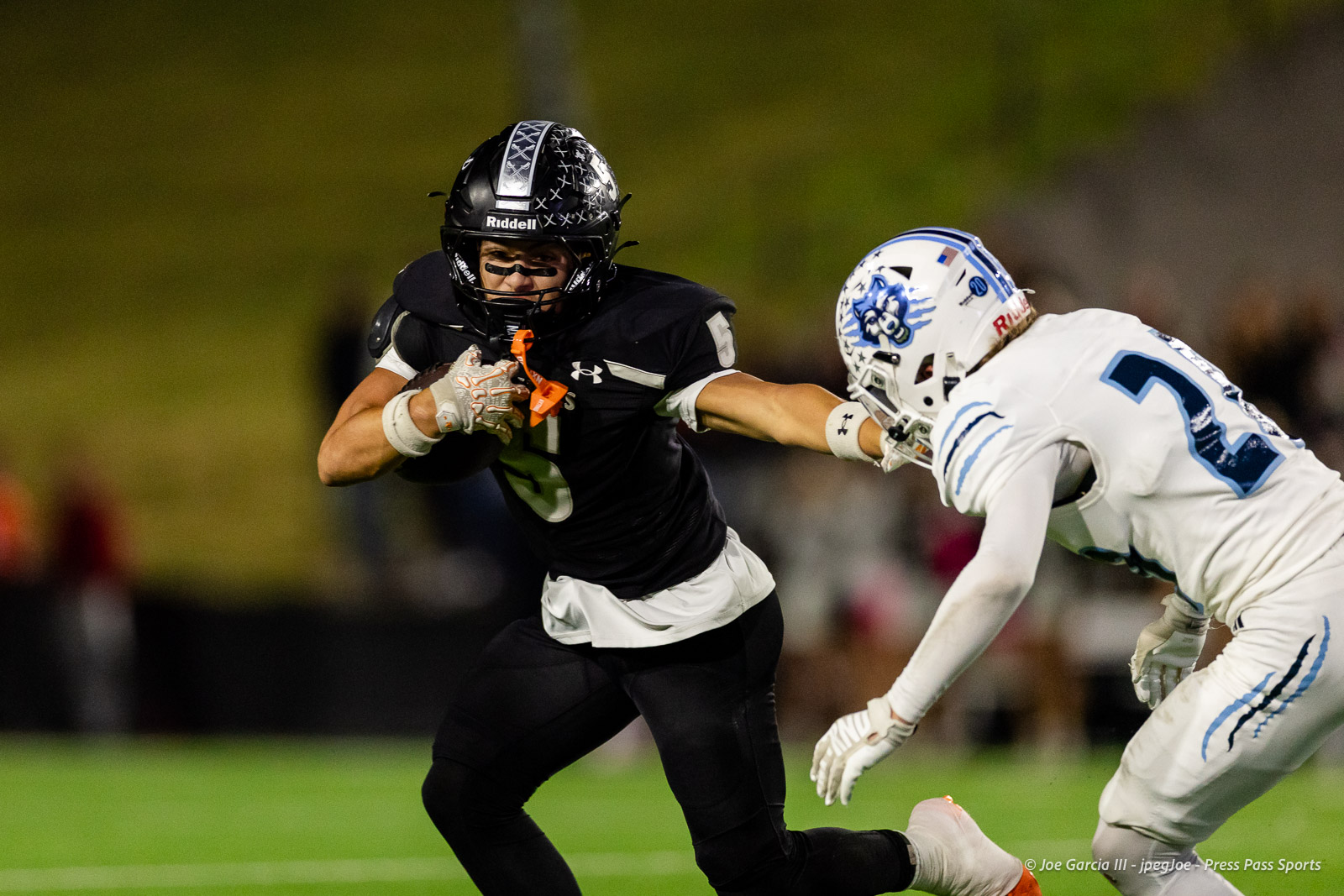 west-plains-vs-randall-2026-jpegJoe-pps-7 | Press Pass Sports American football player in black jersey holds the ball and runs, pursued by a defender in white uniform on a green field.