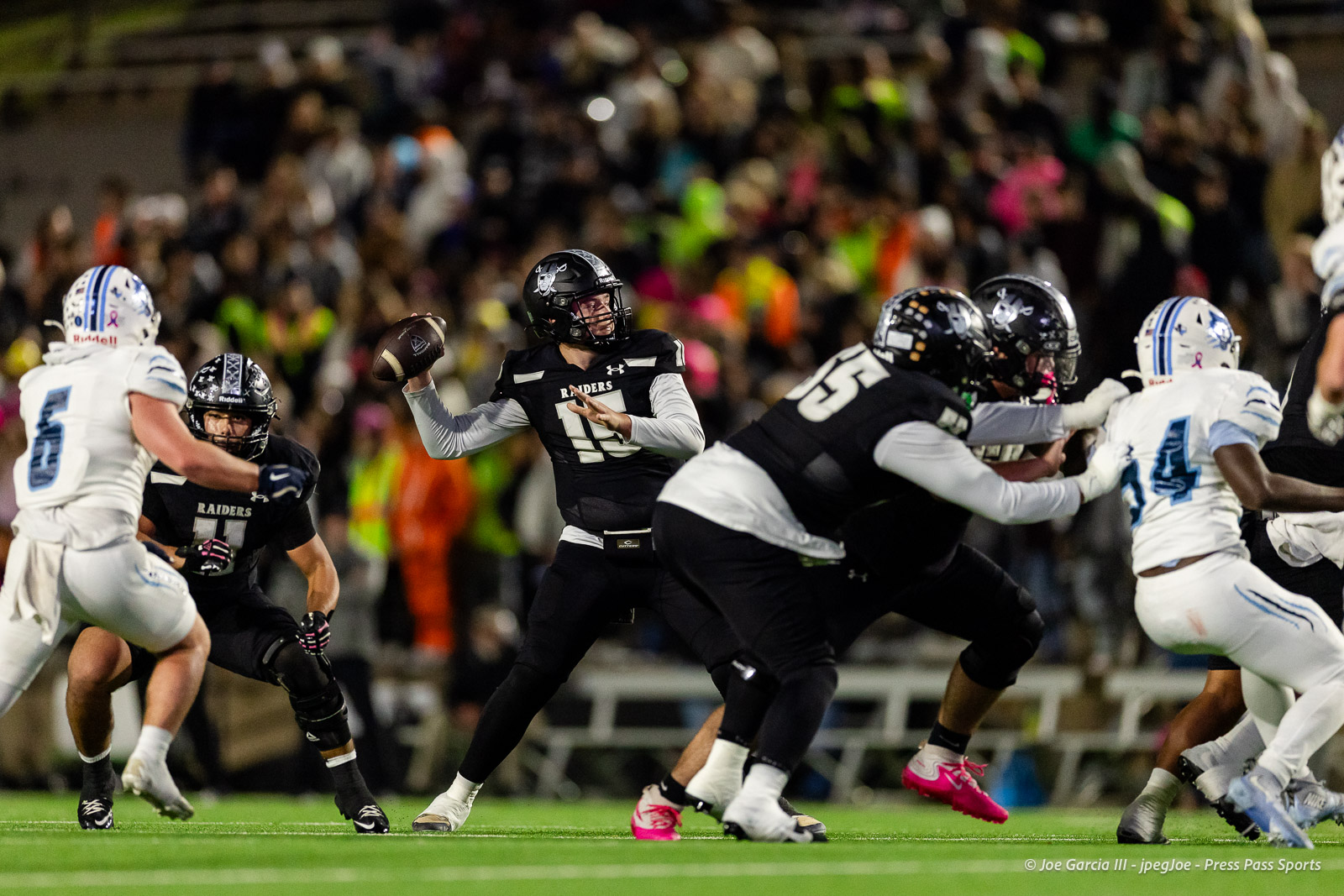 west-plains-vs-randall-2026-jpegJoe-pps-8 | Press Pass Sports Football game action: a Raiders quarterback in black jersey (number 11) throwing a pass while teammates block and white-clad defenders approach behind him, on a crowded night field.