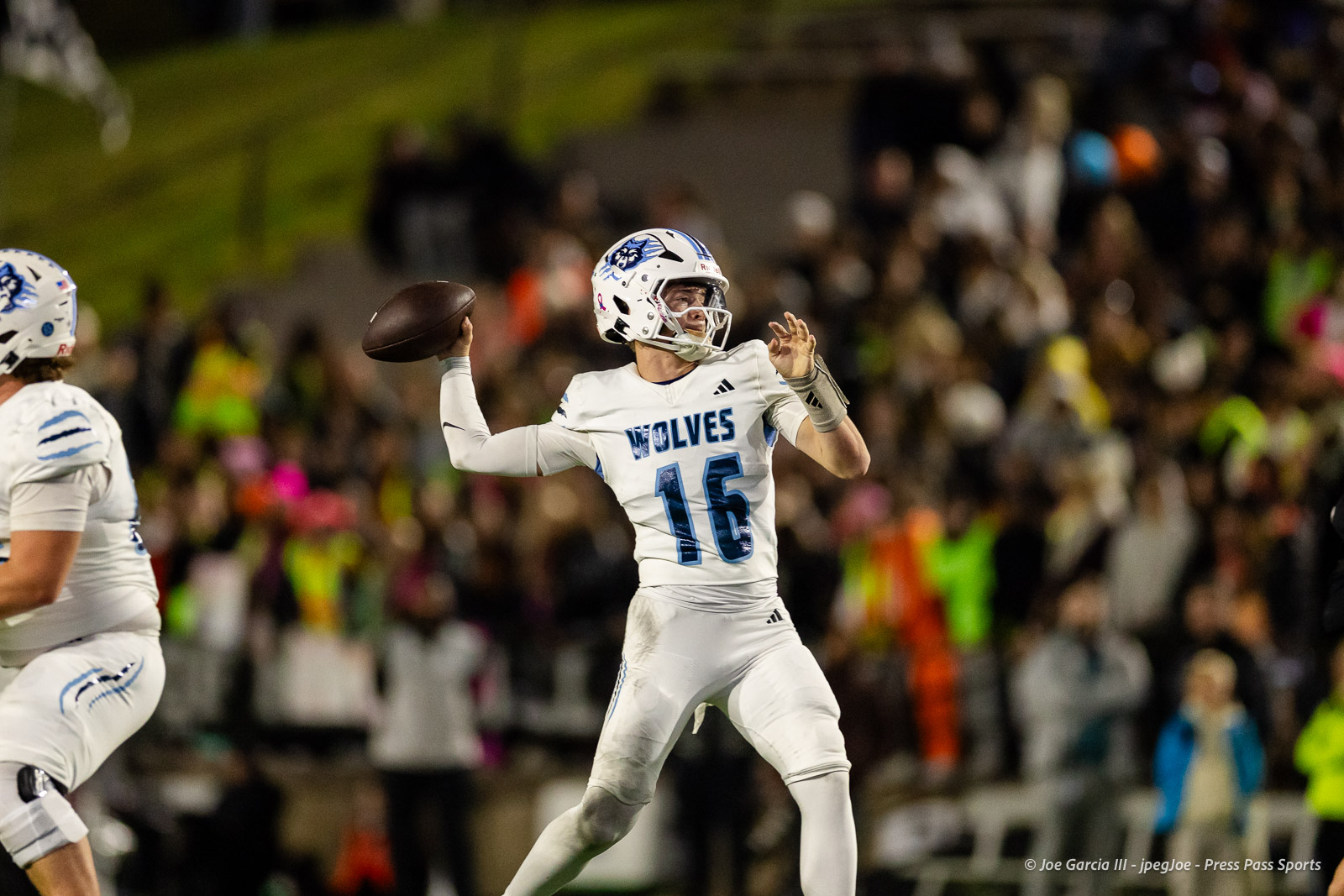 west-plains-vs-randall-2026-jpegJoe-pps-10 | Press Pass Sports Wolves quarterback in white uniform throws a pass during a football game with a crowded stadium in the background, night lighting.