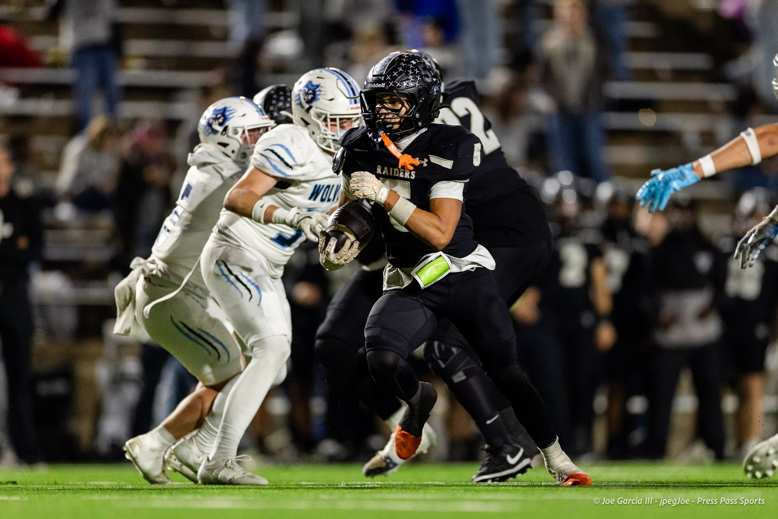 west-plains-vs-randall-2026-jpegJoe-pps-11 | Press Pass Sports Raiders ball carrier wearing black runs forward as white-uniform defenders close in during a nighttime football game on a green field.