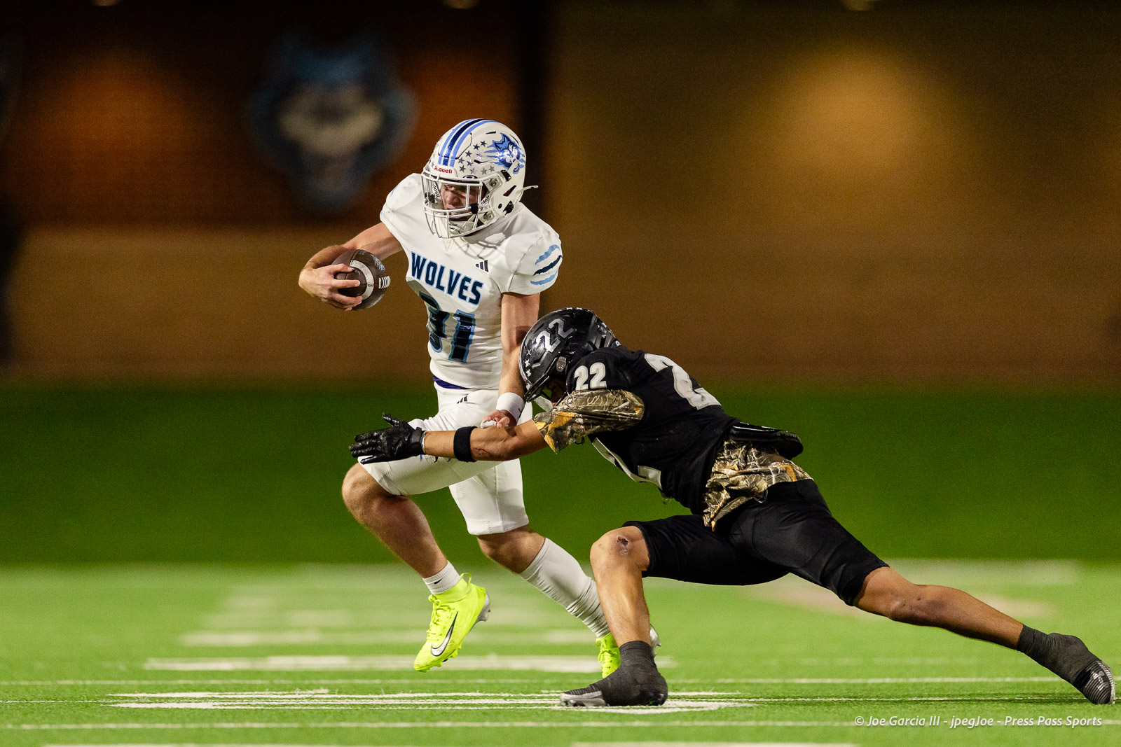 west-plains-vs-randall-2026-jpegJoe-pps-13 | Press Pass Sports White Wolves football player wearing #11 runs with the ball while a defender in a dark uniform dives to tackle him on a brightly lit green field at night.