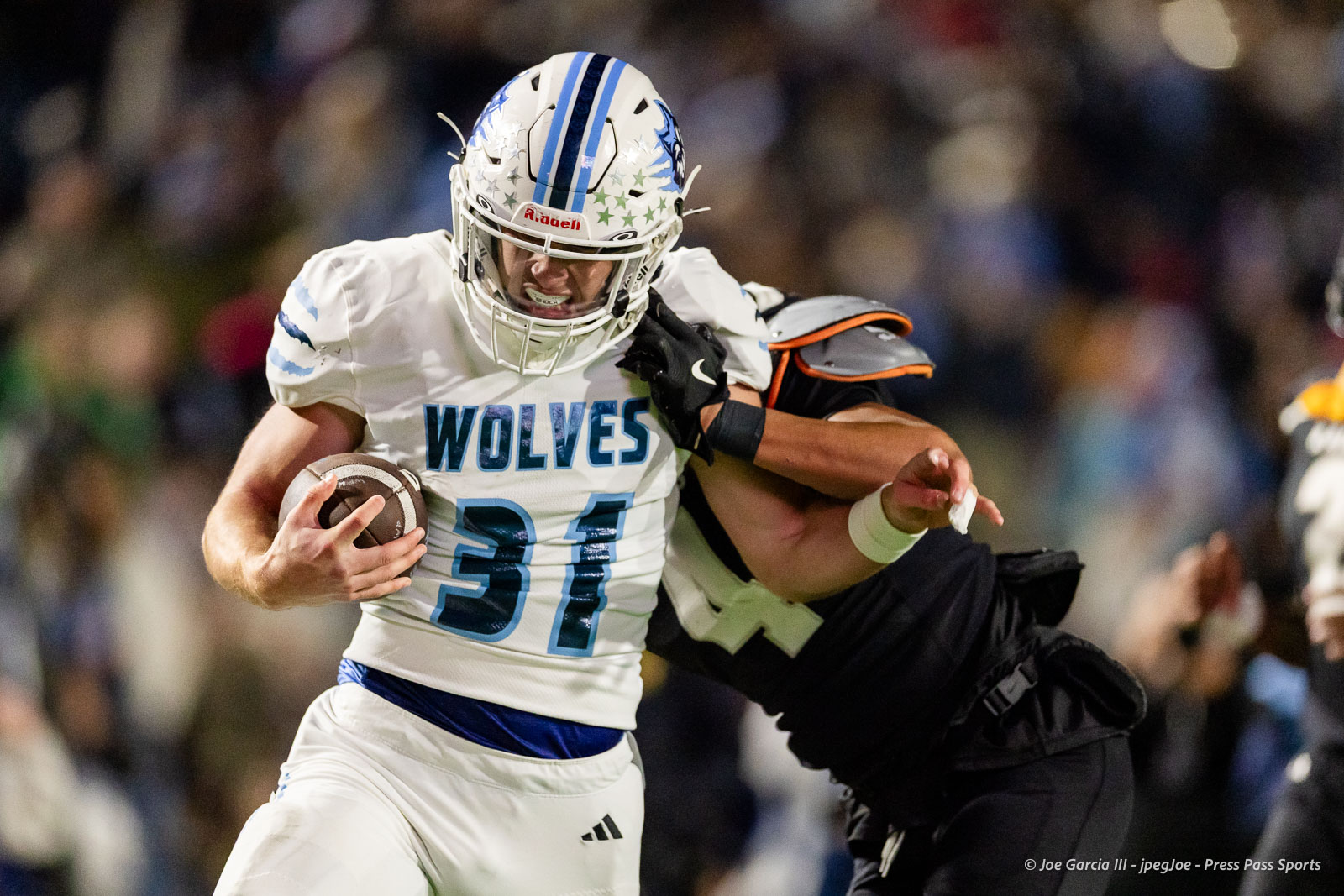 west-plains-vs-randall-2026-jpegJoe-pps-15 | Press Pass Sports American football player in a white Wolves jersey with the blue number 31 runs with the ball as a defender grabs at his arm.