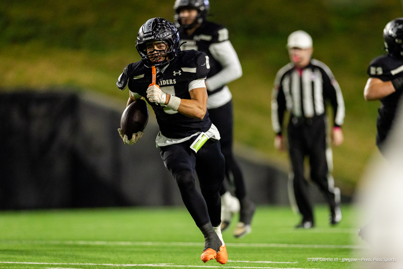 west-plains-vs-randall-2026-jpegJoe-pps-17 | Press Pass Sports Football player in black uniform runs with the ball toward the end zone on a green field, orange cleats visible.
