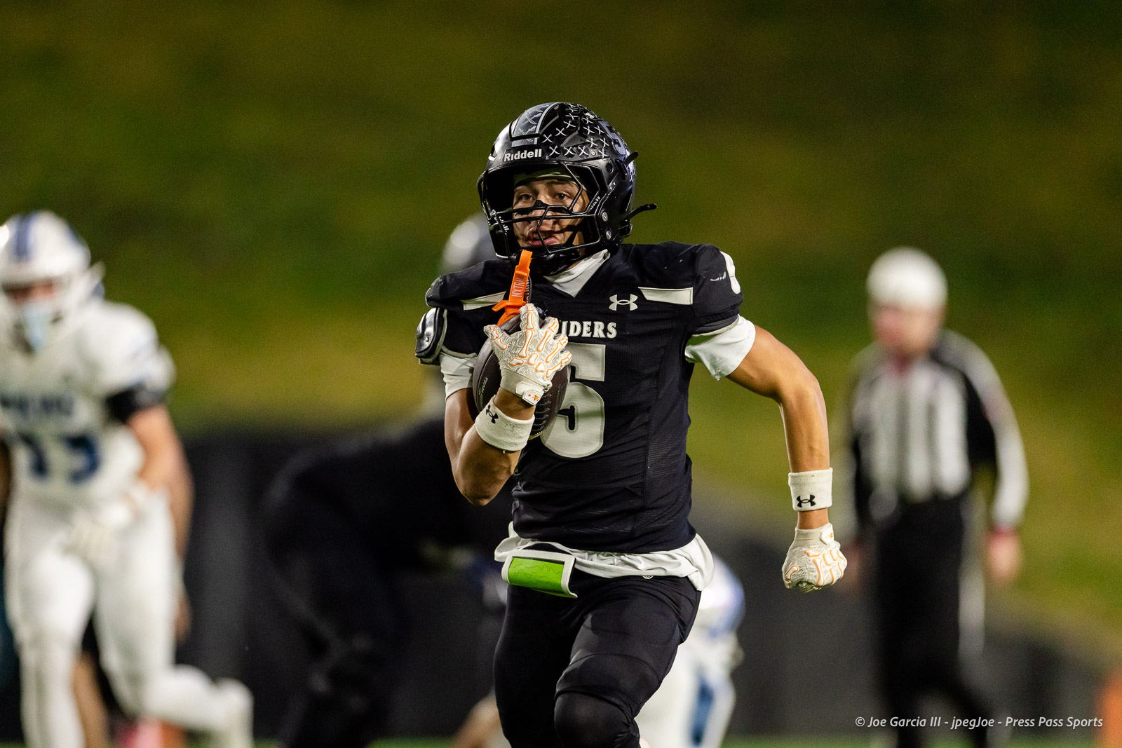 west-plains-vs-randall-2026-jpegJoe-pps-18 | Press Pass Sports American football player in a black uniform sprints with the ball during a night game, orange mouthguard held near his mouth.