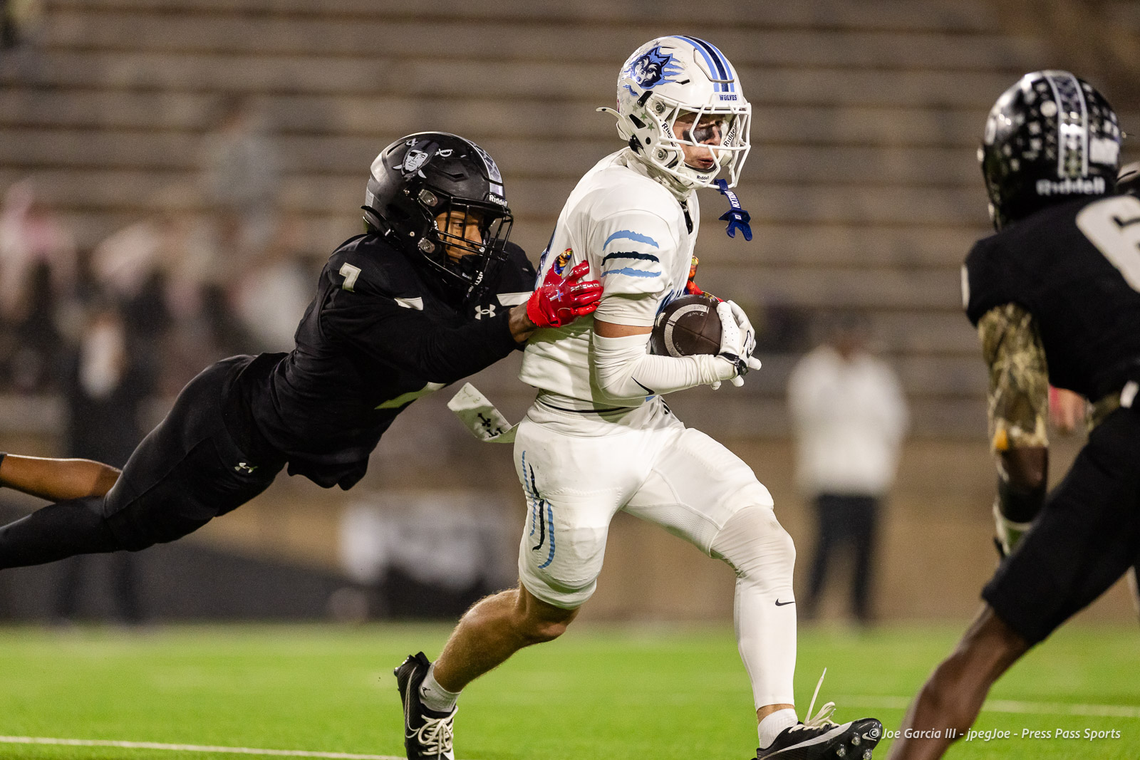 west-plains-vs-randall-2026-jpegJoe-pps-22 | Press Pass Sports Football player in white uniform runs with the ball as a defender in black reaches to tackle him on a grassy field at night.