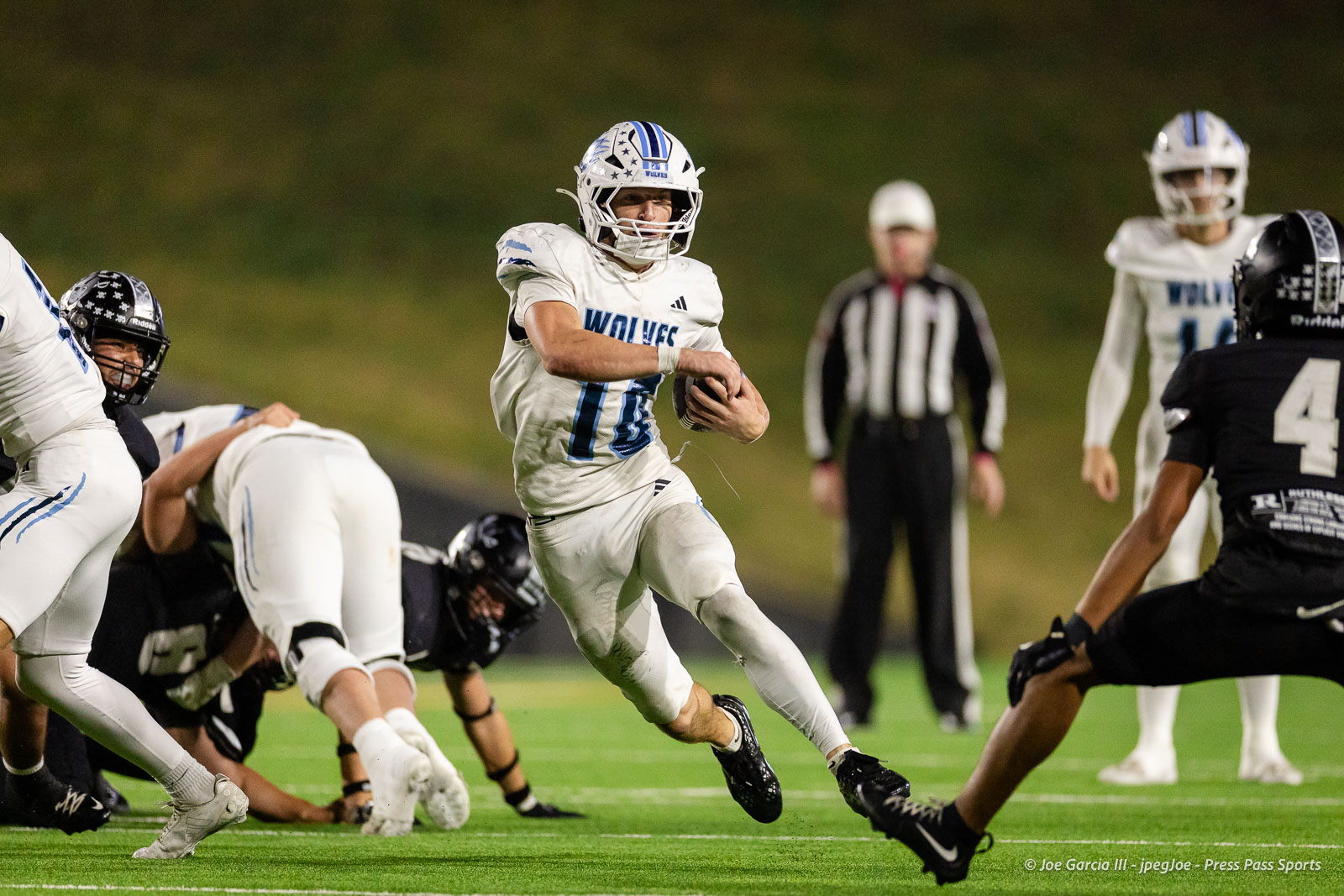 west-plains-vs-randall-2026-jpegJoe-pps-23 | Press Pass Sports Football player in white with blue numbering runs with the ball on a green field toward the right, pursued by others.