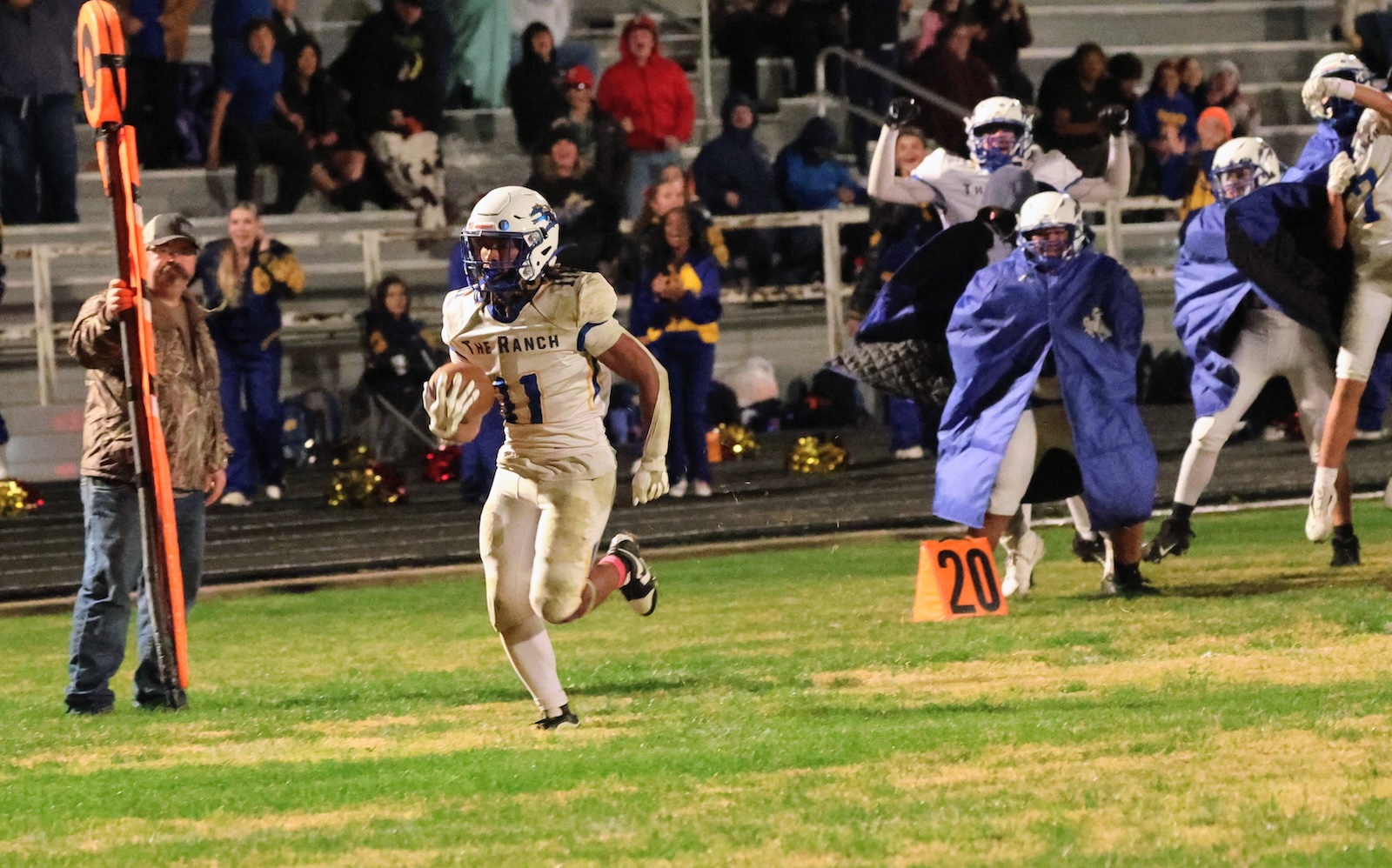 Football player in white jersey #11 carries the ball along the sideline while spectators watch from the bleachers.