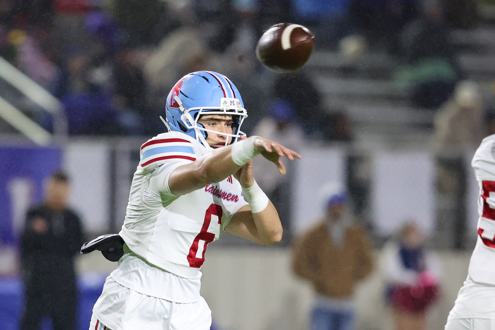 Seabolt Chase-19019 | Press Pass Sports Quarterback in white and blue football uniform throwing a pass in a stadium crowd behind him.