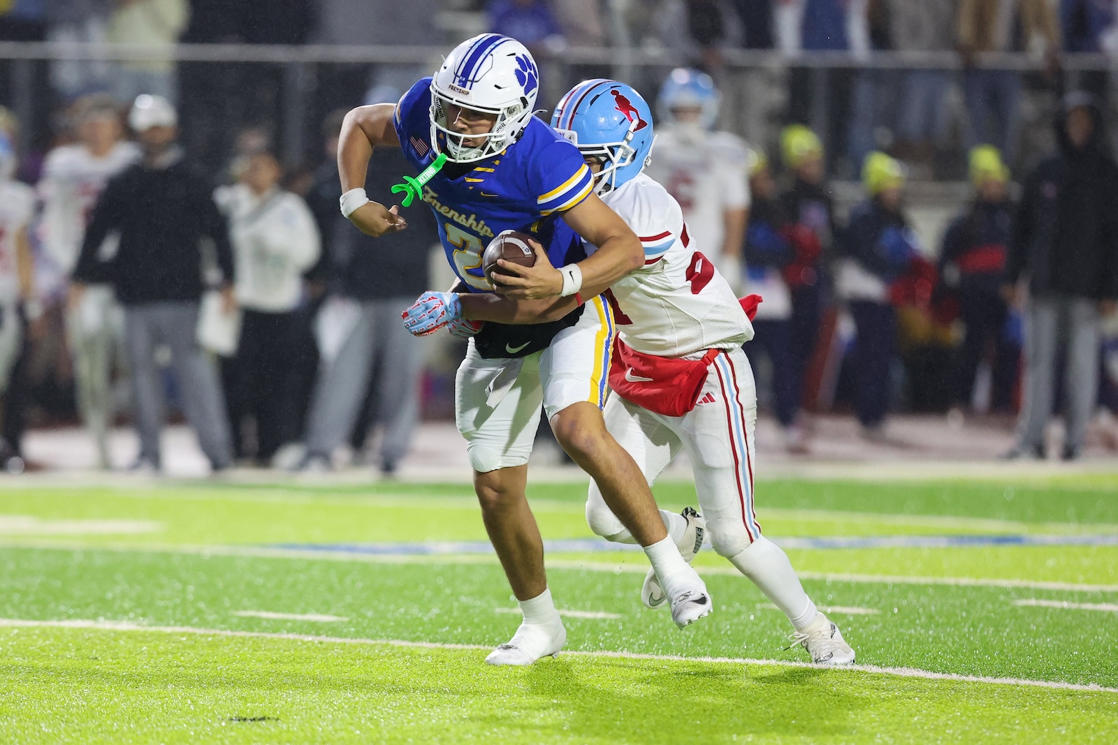 Seabolt Chase-19384 | Press Pass Sports Football action: a player in blue and yellow runs with the ball while a pursuing defender in white and red closes in on a bright green field with blurred crowd in the background.