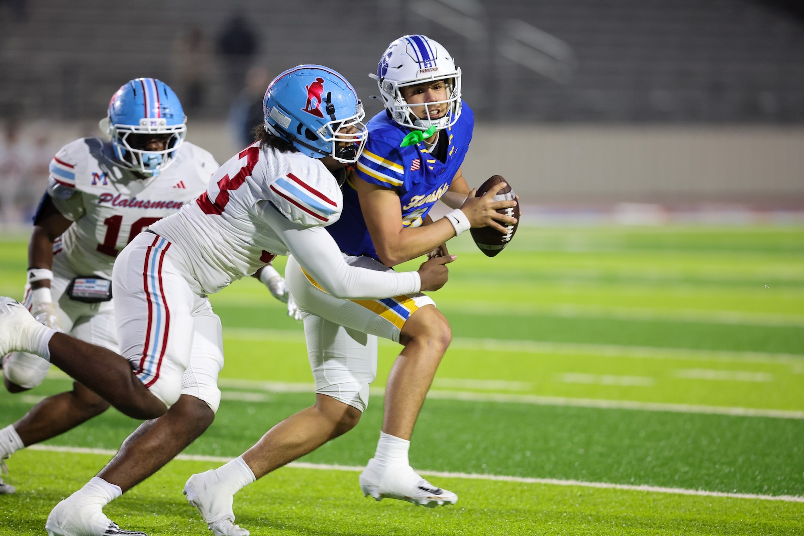 Seabolt Chase-19435 | Press Pass Sports Blue-uniform quarterback holds the football and dodges a tackle from a white-uniform defender on a green turf field on a football field.