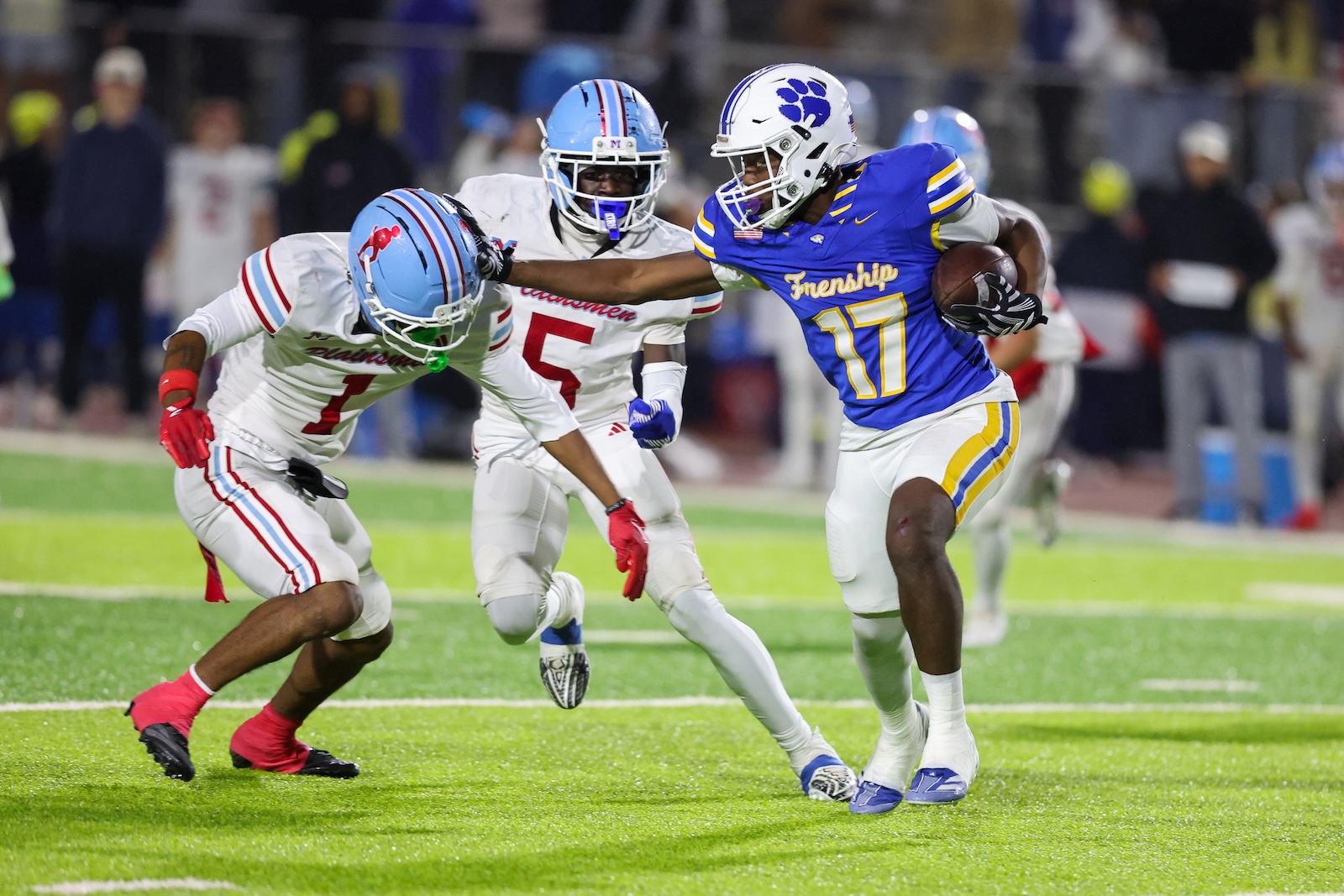 Seabolt Chase-19482 | Press Pass Sports Football player in blue #17 runs with the ball, pursued by white-jersey opponents on a green field.