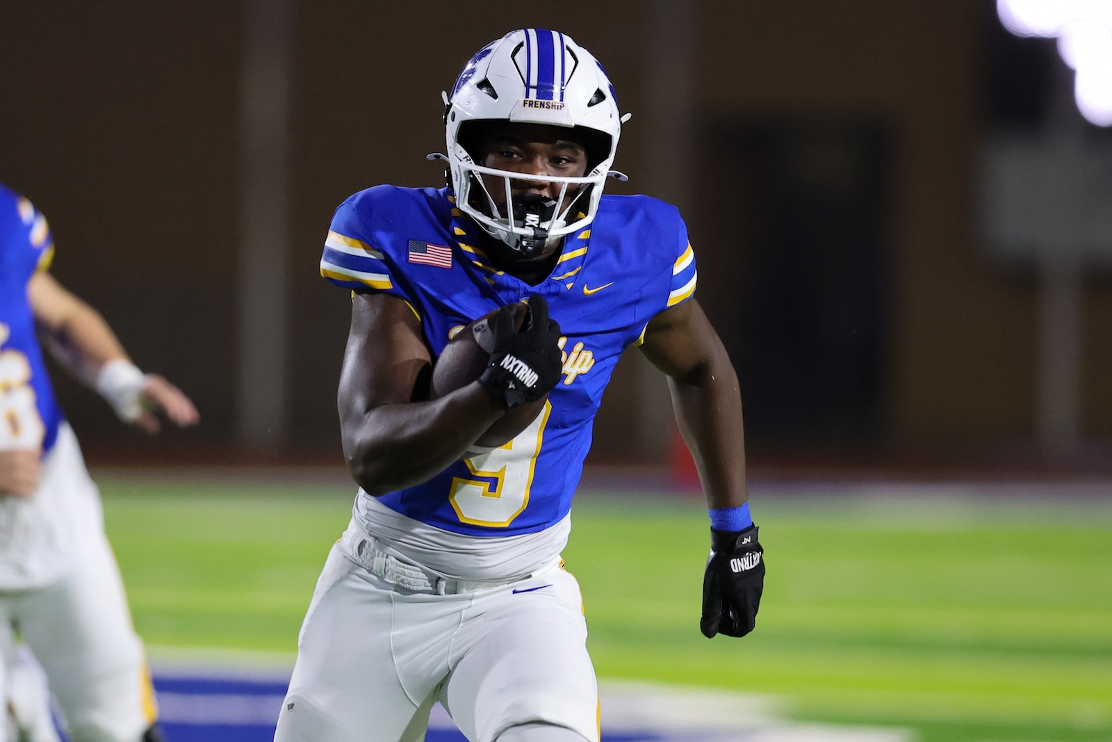 Seabolt Chase-19568 | Press Pass Sports American football player in a blue and yellow uniform running with the ball during a game, wearing a white helmet and black gloves