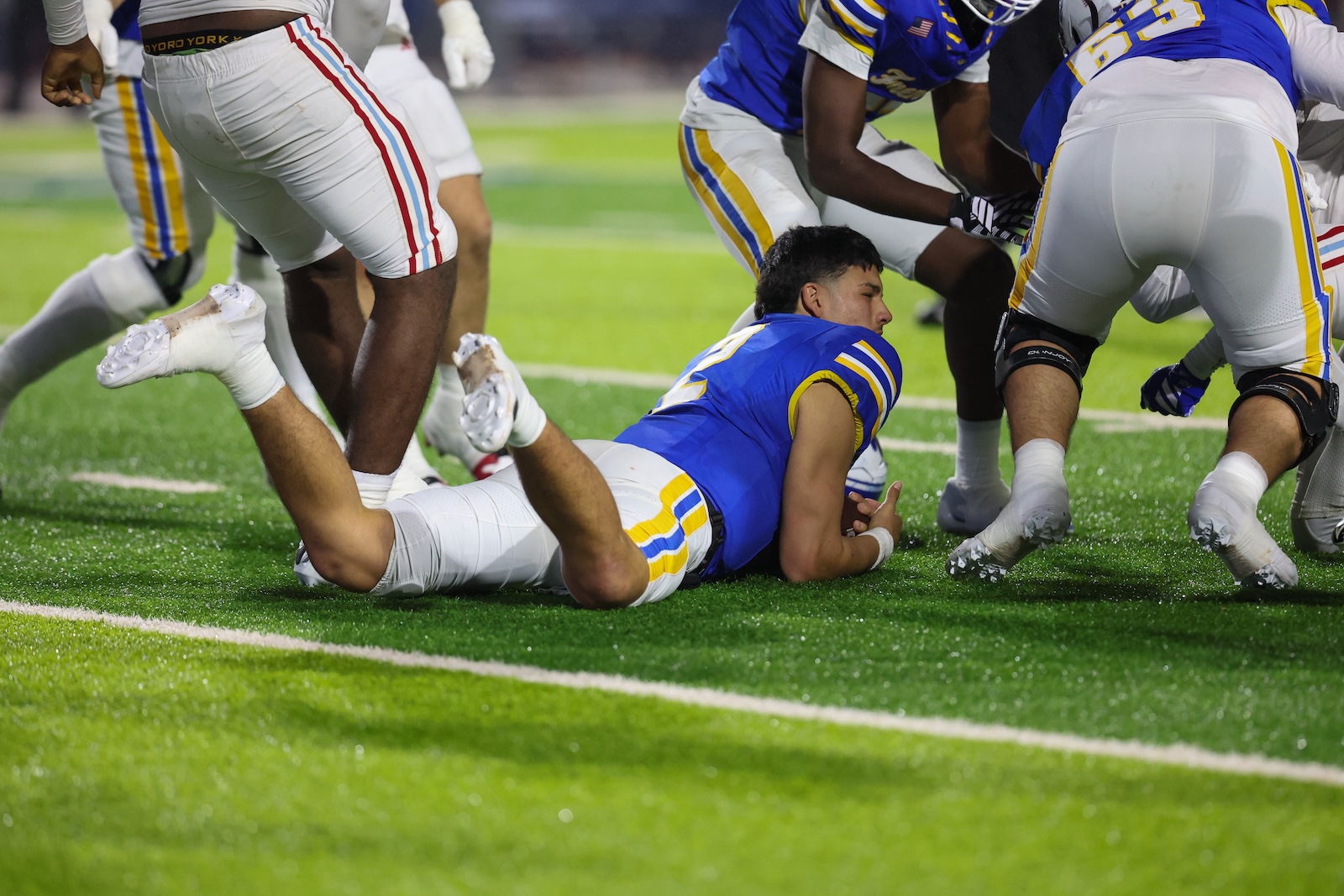 Seabolt Chase-19619 | Press Pass Sports Football players collide on a green turf; a blue-uniformed player lies on his stomach as teammates surround during the play