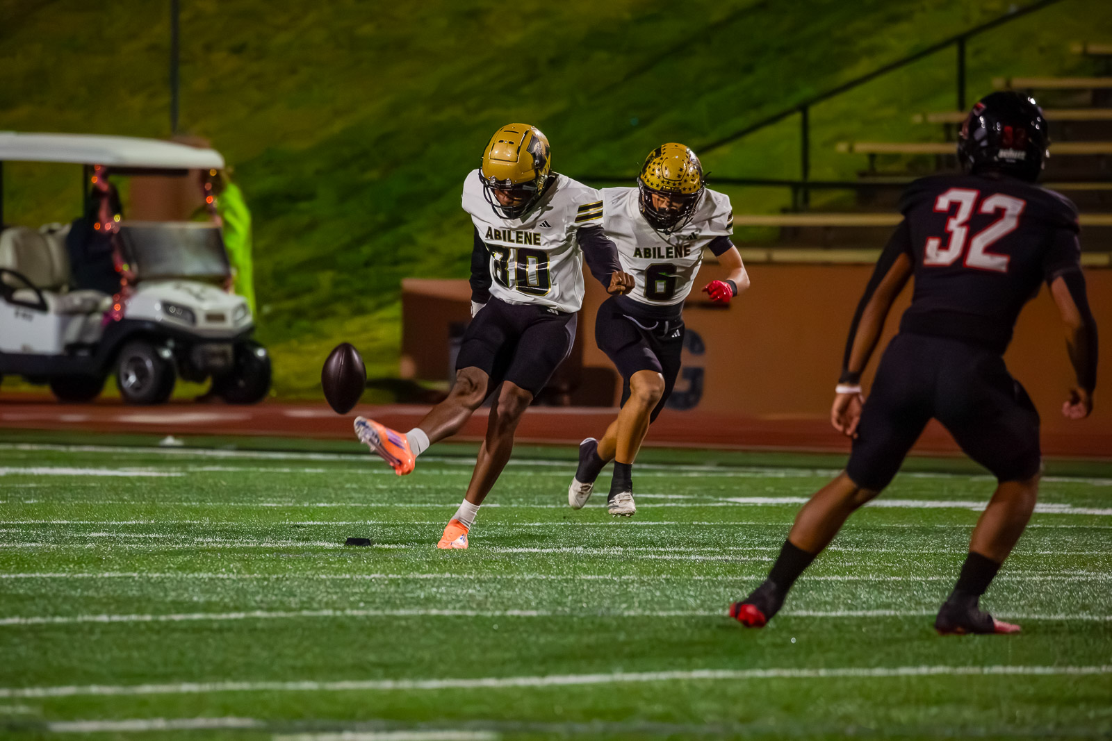 Two Abilene football players in white and gold chase a loose football on a turf field while a defender in black watches nearby.](https://)