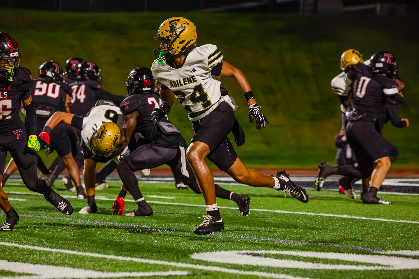 Male football player in a white Abilene jersey (#4) runs with the ball during a nighttime game on a green turf field.