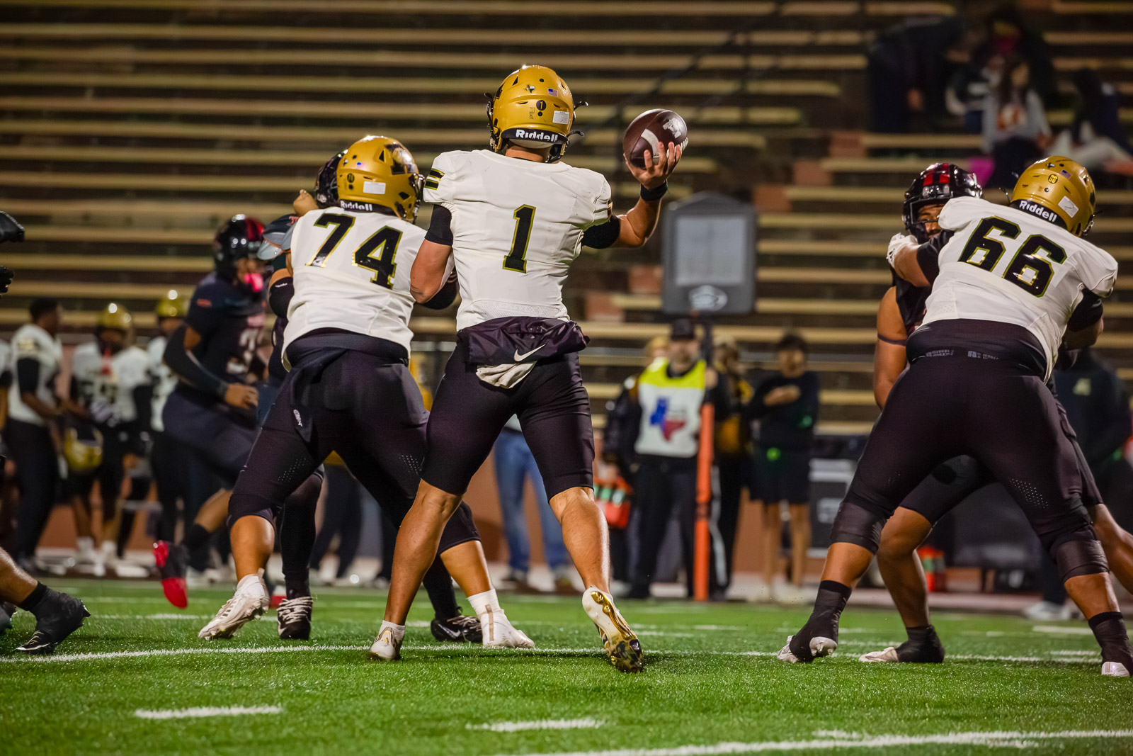Quarterback in white jersey (No. 1) prepares to throw as teammates block on a football field.