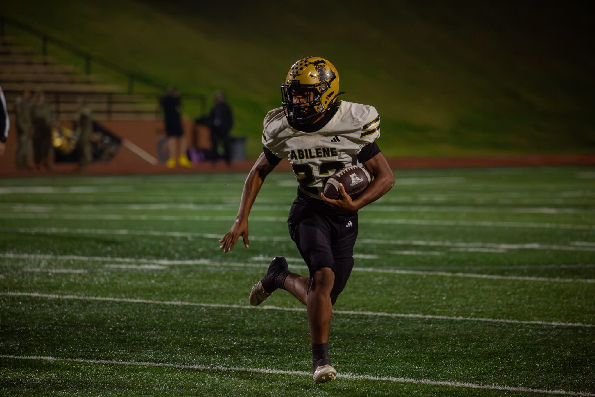 Football player in a white Abilene jersey runs with the ball on a night game field.
